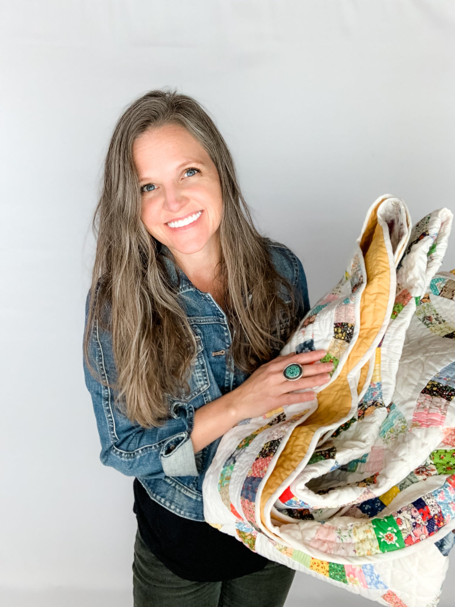 Tamara Darragh holding a vintage patchwork quilt in front of a white background.