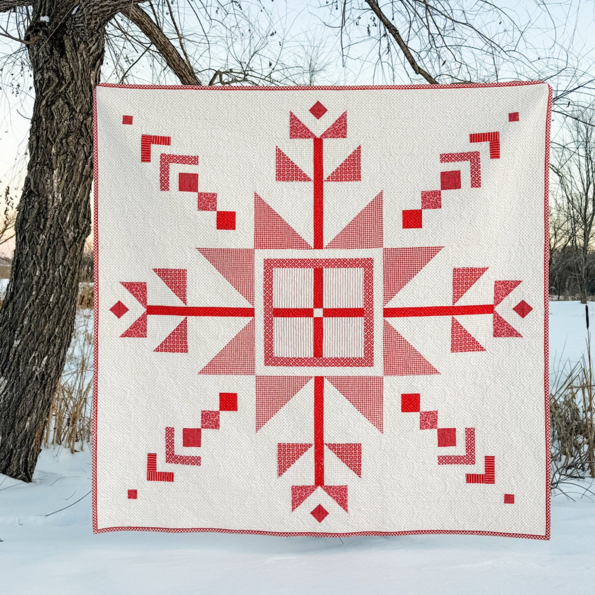 Red geometric quilt on a snowy landscape with trees