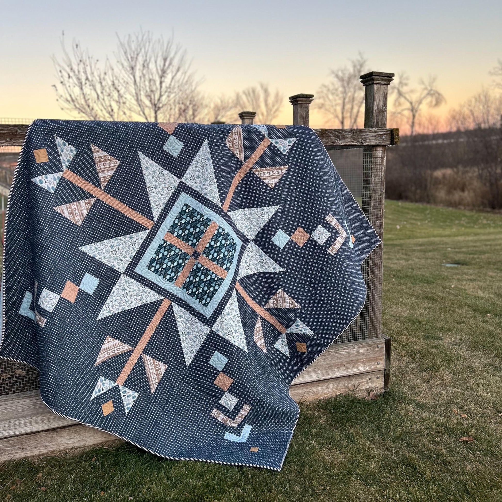 Quilt with geometric pattern draped over a wooden structure outdoors