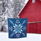 Blue quilt with geometric pattern in front of a red barn during snowfall