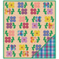 A quilted blanket or quilt pattern featuring a grid of colorful floral motifs on a beige background with a green border. The bottom-right corner is folded over to reveal a plaid pattern in shades of blue, green, purple, and pink.