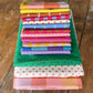 A stack of colorful folded fabric pieces with various patterns including stripes, polka dots, and checks, displayed on a rustic wooden surface.