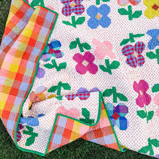 A colorful quilted blanket with a floral patchwork pattern and a plaid backing, laid out on green grass.