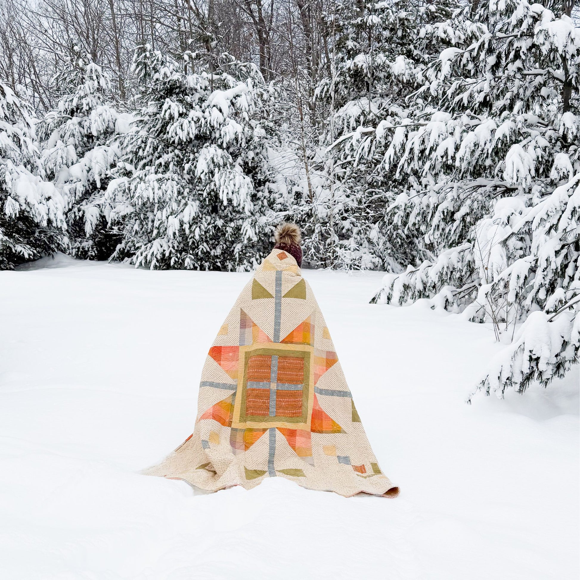 Person wrapped in a colorful quilt standing in a snowy forest
