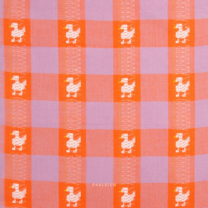 A close-up of a woven textile pattern featuring alternating lavender and orange checkered squares, with small white duck motifs centered on the orange squares.