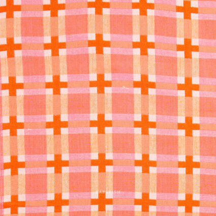 A close-up of a woven textile pattern featuring orange plaid lines with orange crosses over a pink and white background.