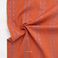A close-up of orange fabric with a repeating lavender floral pattern and thin vertical stripes, gathered in the center to show texture. The brand name 'FABLEISM' is printed in white near the bottom.