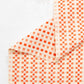 Folded fabric with orange and beige checkered pattern on a textured white background