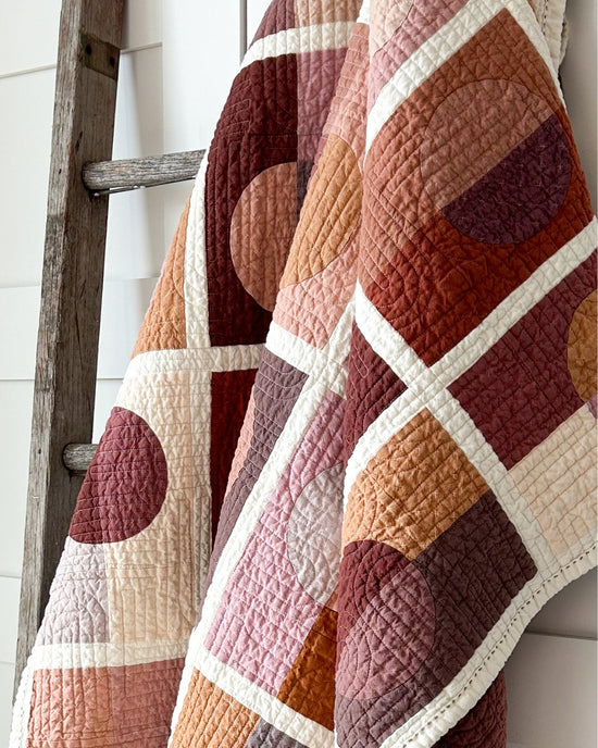 Full Circle Quilt hanging on the side of a vintage wooden ladder in front of a white closet door.