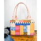 A Patchwork Pockets version of the Maggie Poppins Tote made with yarn dyed wovens in pink, blue, yellow, red, and olive sitting on a wooden bench with a white background.