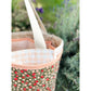 A close up of a pink, red, green, and white Maggie Poppins Tote in front of lavender bushes.