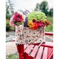 A Maggie Poppins Tote made with pink, red, black and white fabric filled with a garden bouquet, sitting on a red adirondack chair.