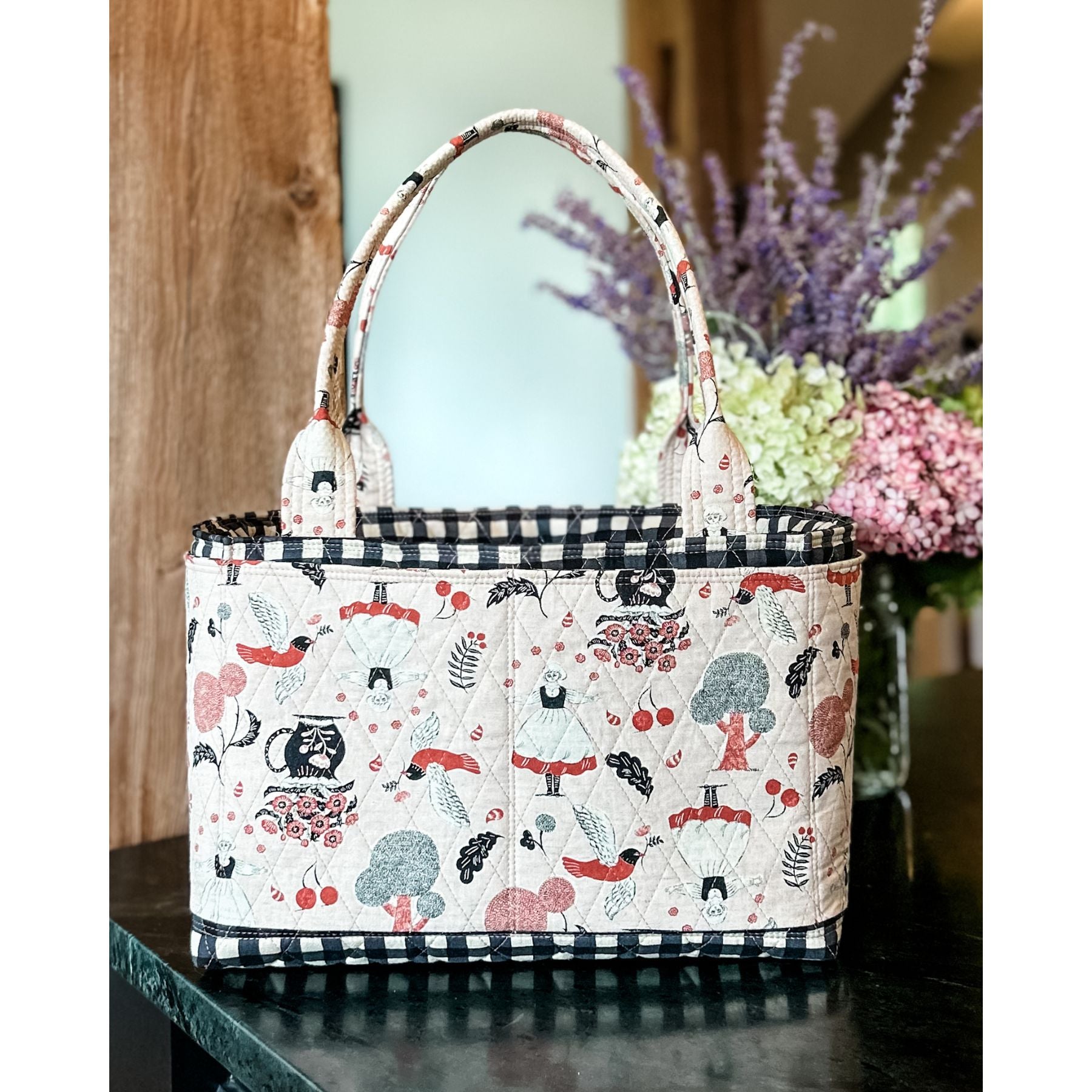 A Maggie Poppins Tote made with pink, red, black and white fabric sitting on a black stone countertop.