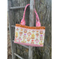 A Maggie Poppins Tote made in pink, brown, purple, yellow with floral fabric and embroidery detailing, hanging on a vintage ladder against a tree.