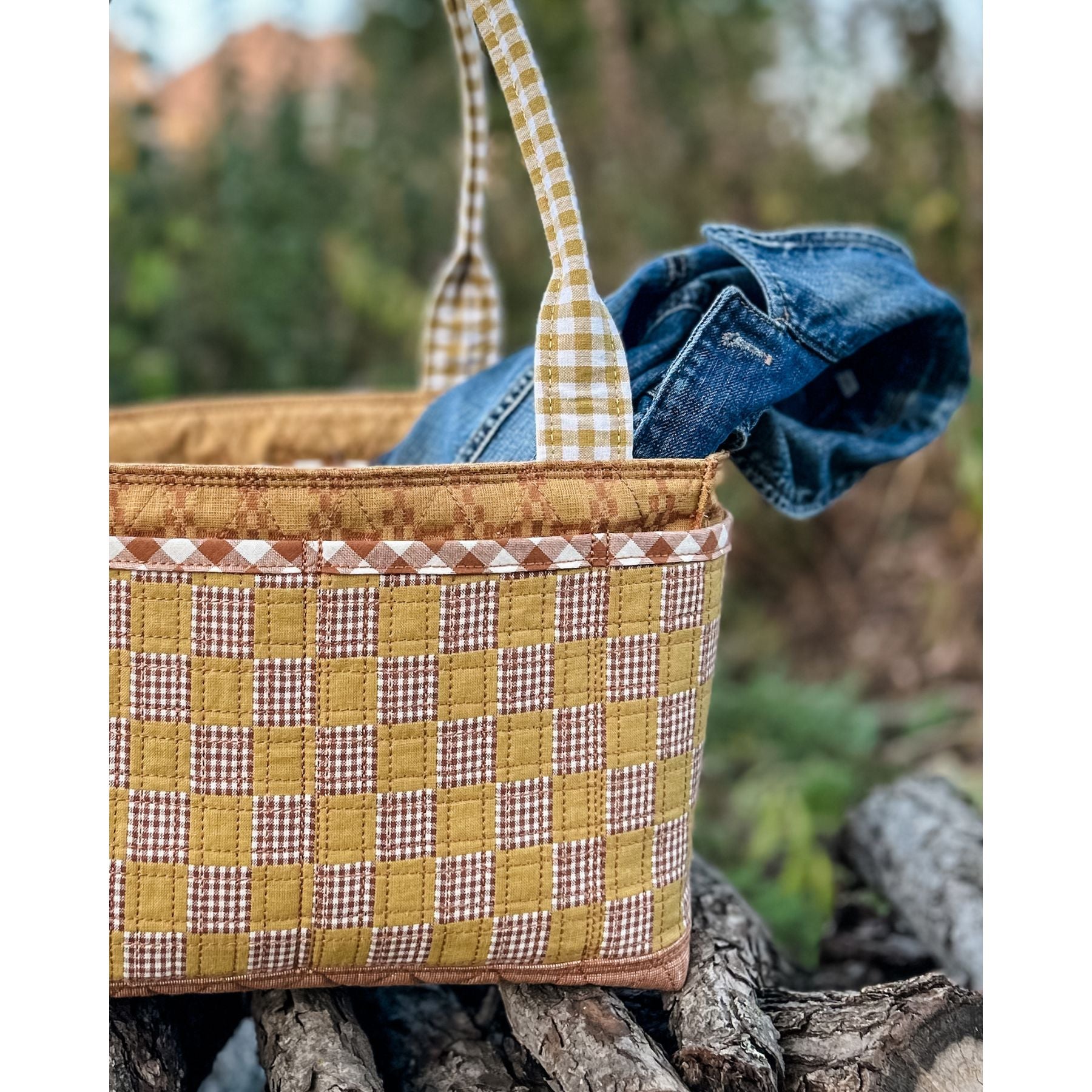 Maggie Poppins Tote made in brown, yellow, and white sitting on wood pile with denim jacket inside.