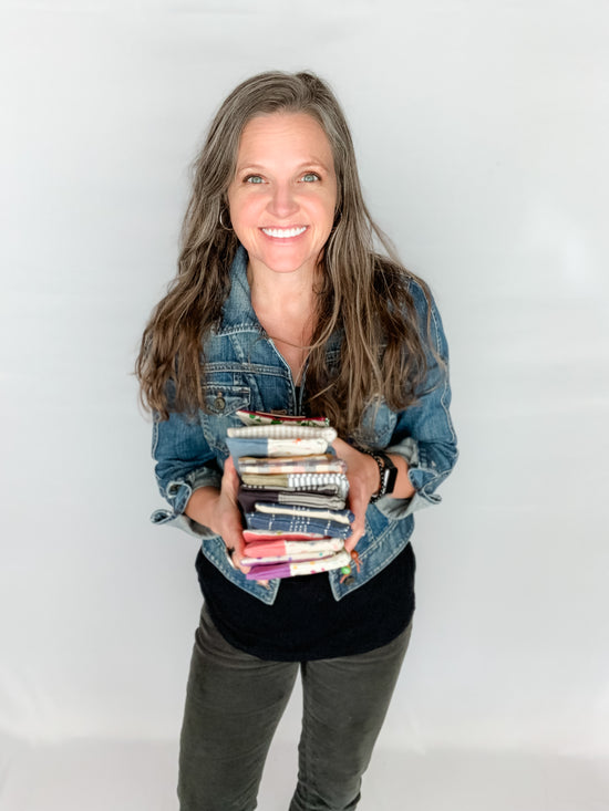 Tamara Darragh holding a stack of handmade zipper pouches in front of white wall.